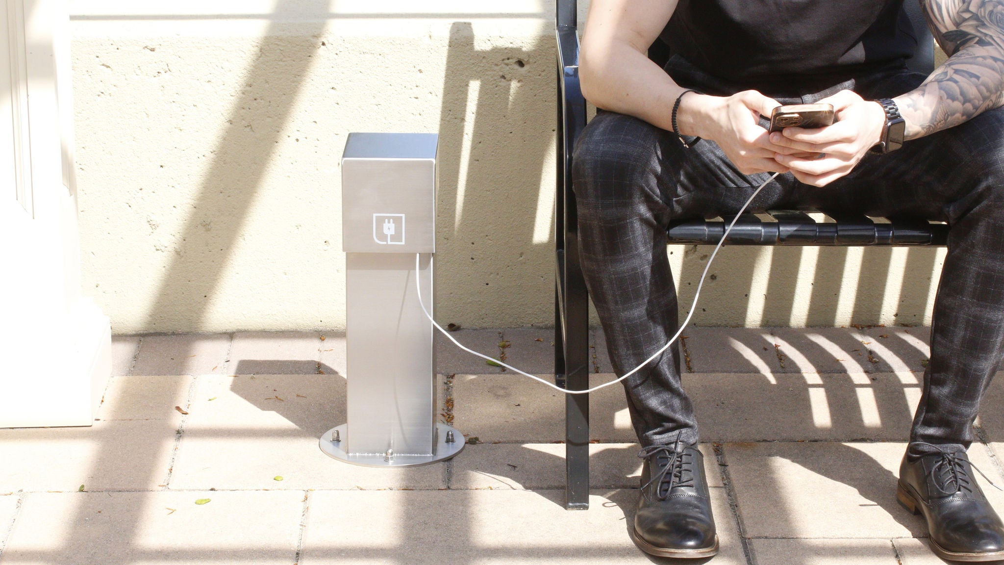 Un hombre sentado en un banco cargando su teléfono con un pedestal de alimentación